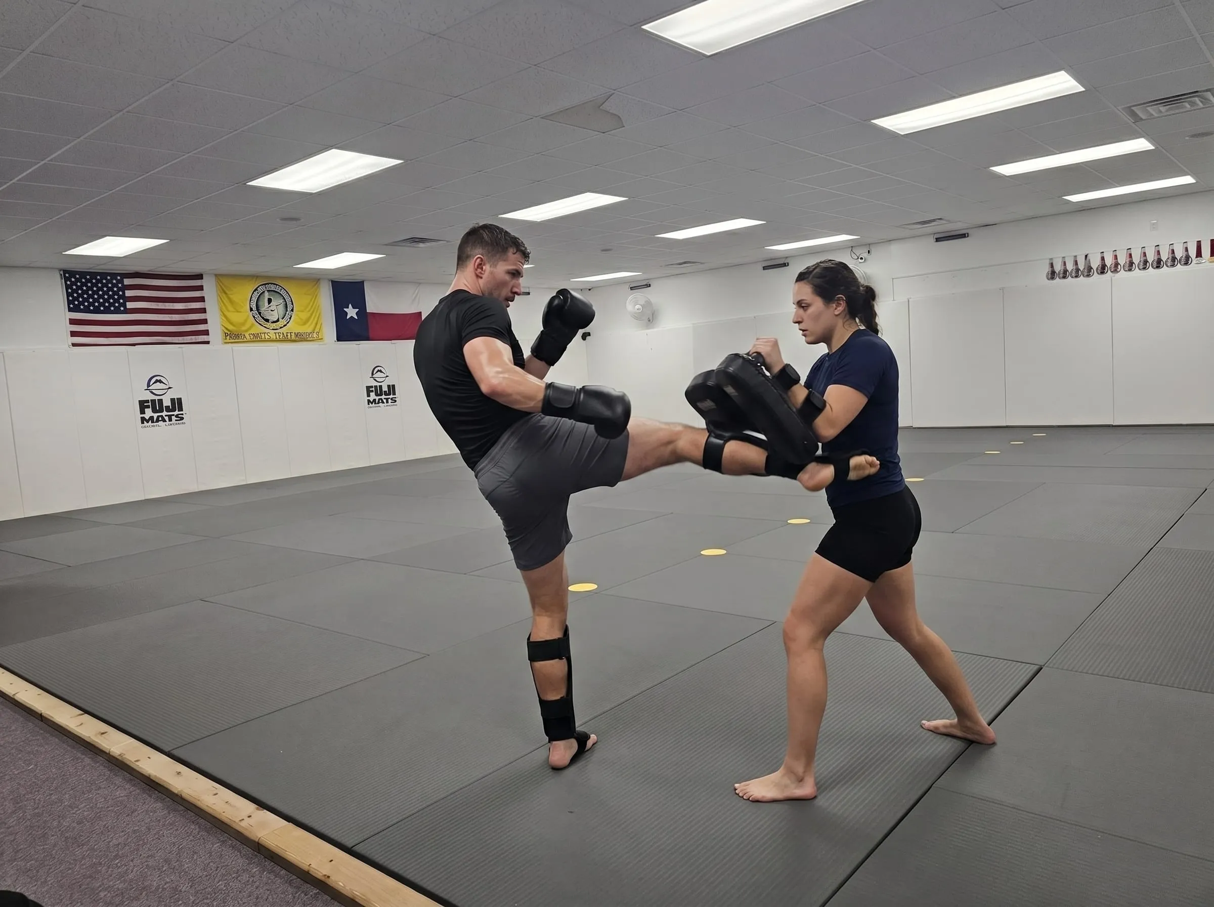 An adult throwing a round kick into a Thai pad during kickboxing class at Dynamic Martial Arts